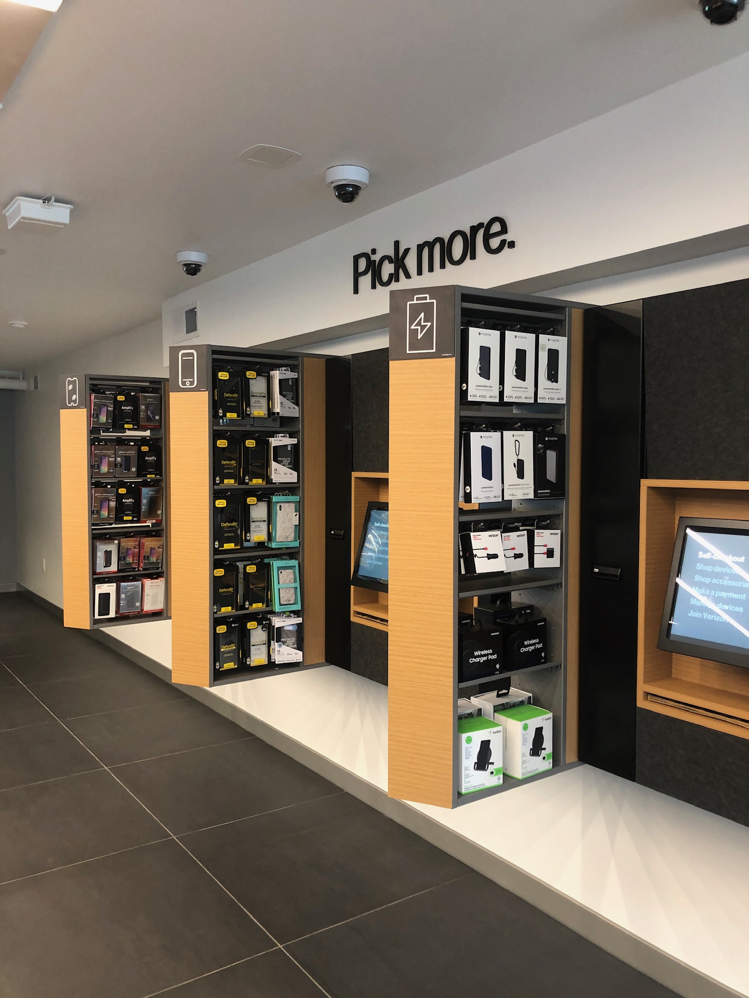 The Express Store accessory wall and self-checkout kiosk, with a 'Pick more' display of cases, chargers, and accessories