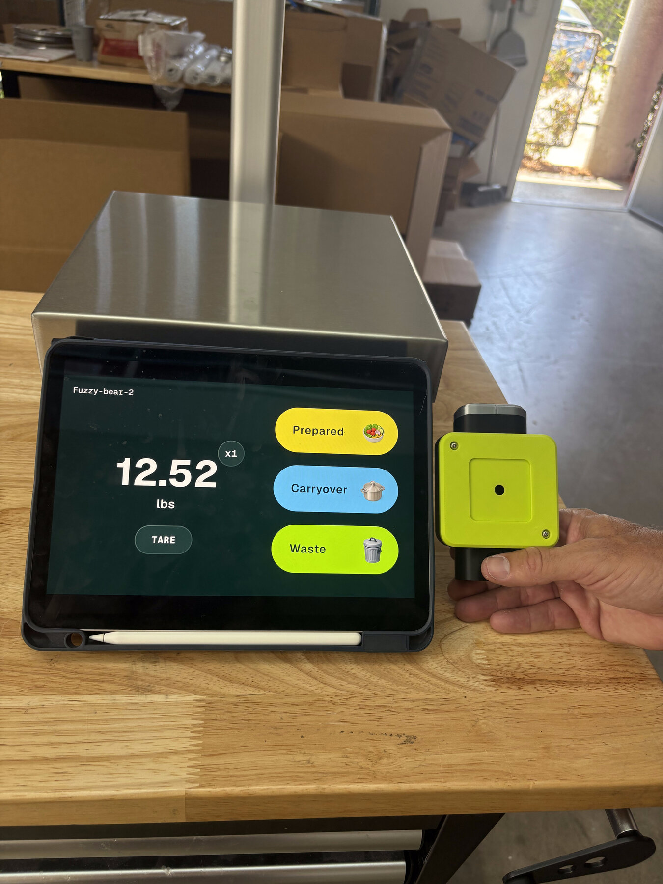 The StreamLine scale prototype held next to an iPad running the scale UI, comparing the device's physical color to the on-screen Waste/Carryover/Prepared colors